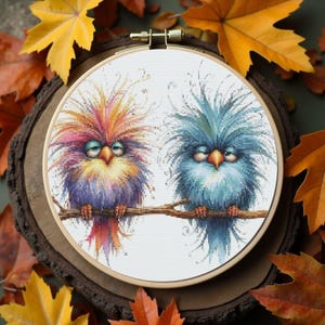 K&ouml;nnte beinhalten: Ein Kreuzstich-Stickrahmen mit zwei skurrilen V&ouml;geln auf einem Ast. Die V&ouml;gel haben farbenfrohes, flauschiges Gefieder in Lila, Orange, Gelb und Blau. Der Hintergrund umfasst Herbstbl&auml;tter.