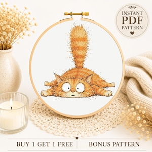 Op de afbeelding: Een kruissteekpatroon met een oranje cyperse kat met grote ogen die plat ligt met de staart recht omhoog in de lucht. Het ontwerp wordt weergegeven in een ronde houten borduurring. De tekst INSTANT PDF PATTERN is zichtbaar in de hoek.