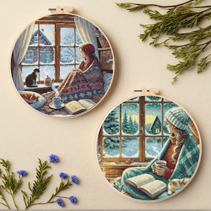 Puede incluir: Dos aros de bordado redondos presentan escenas invernales. Uno muestra a una persona envuelta en una manta junto a una ventana con un gato, el otro a una persona con una taza de té. Ambos tienen un tema acogedor y nevado.