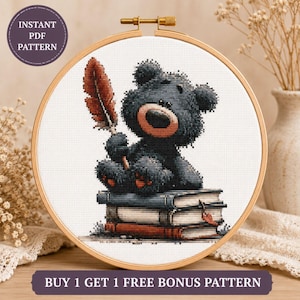 May include: A cross-stitch pattern in a wooden embroidery hoop featuring a dark gray teddy bear sitting on a stack of three books. The bear holds a large red feather quill. Text on the image reads INSTANT PDF PATTERN and BUY 1 GET 1 FREE.