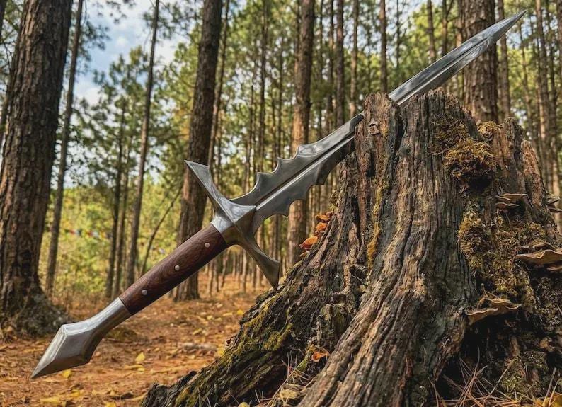 May include: A detailed, silver-colored sword with a wooden handle, resting on a tree stump in a forest. The blade has a unique, serrated design. The handle is a dark brown color with silver accents.