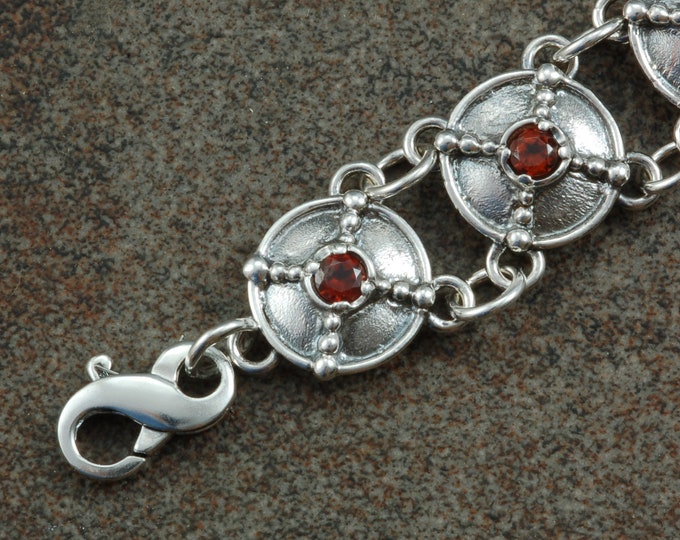 Sterling silver link bracelet with light patina set with garnets and decorated with bead work.