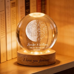 May include: A clear glass sphere with a map design and the names "Jennifer & William" and date "04.15.2020" engraved on it. The sphere sits on a wooden base with the words "I love you forever". The sphere is illuminated.