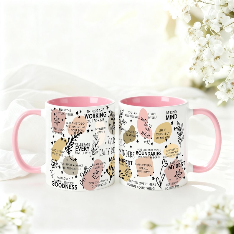 May include: Two white ceramic mugs with pink handles and interiors. The mugs are decorated with inspirational phrases and floral designs in black, gold, and pink. The text includes phrases like "Be Kind Mind" and "Celebrate Every Single Win."