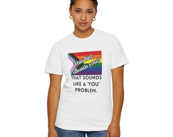 以下が含まれることがあります： 虹色の旗のデザインと「This flag offends you? That sounds like a 'you' problem」というテキストがプリントされた白いTシャツ。ジーンズを履いた人が着ています。
