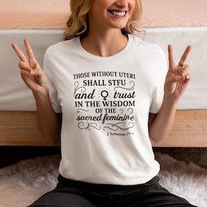 May include: White t-shirt with the text "THOSE WITHOUT UTERI SHALL STFU and trust IN THE WISDOM OF THE sacred feminine" in black script. The shirt also includes the text "2 Fallopians 24:7".