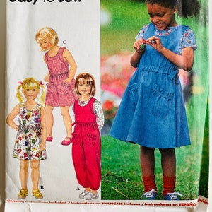 May include: Simplicity sewing pattern 7211 for children's clothing. The pattern includes instructions for dresses and a jumpsuit. The image shows illustrations of the finished garments, including a red gingham dress, a floral print dress, and a red jumpsuit.