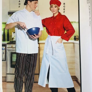 May include: McCall's R11621 sewing pattern envelope featuring illustrations of chef uniforms. The pattern includes a white short-sleeve chef coat, a red long-sleeve chef coat, striped pants, a white apron with a front slit, and two styles of chef hats.