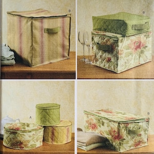 May include: Four fabric storage boxes in various sizes and designs. One box has vertical pink stripes on a beige background. Another has a floral pattern with pink and green flowers. Two round boxes and a square box with a green quilted pattern.