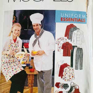 May include: A McCall's M2233 Uniform Essentials sewing pattern envelope featuring illustrations of chef jackets, pants, aprons, and hats. The cover displays a person in a white chef coat and hat with checkered pants, and another in a chili pepper print apron.