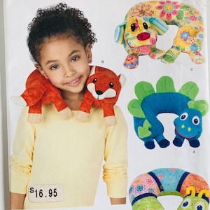 May include: Simplicity pattern 1518 featuring various neck pillow designs. The image shows a child wearing a fox-shaped neck pillow. Other designs include a dog, a dinosaur, and a caterpillar. The pattern is one size.