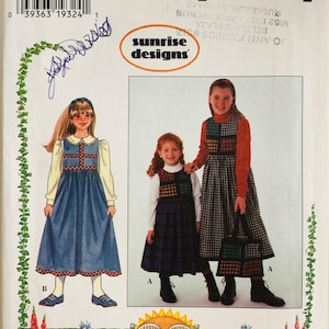 May include: Simplicity sewing pattern featuring girls' dresses. The pattern includes illustrations of the dresses, with a blue dress on the left and two girls wearing dresses with plaid accents on the right. The pattern is labeled "sunrise designs".