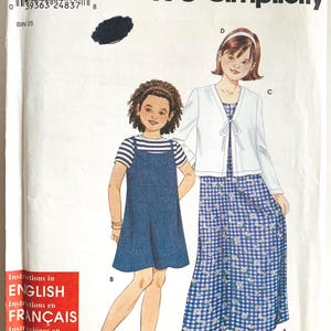 May include: A vintage sewing pattern titled "It's SO EASY it's Simplicity." The pattern features illustrations of two young girls wearing dresses. One girl is in a blue denim dress over a striped top, and the other is in a blue and white floral dress.
