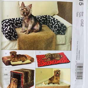 May include: A sewing pattern envelope for pet beds and crate covers featuring five variations labeled A through E. The images display dogs on a leopard print crate cover, a plaid bolster bed, a bone-patterned sofa guard, a corner mat, and a paw print mat.