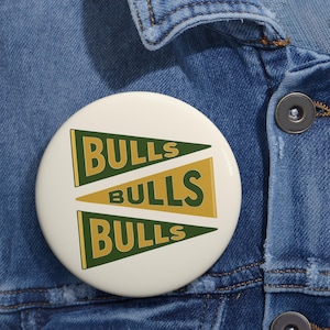 May include: A white button with the word "BULLS" in green and gold pennant shapes. The button is pinned to a blue denim jacket.