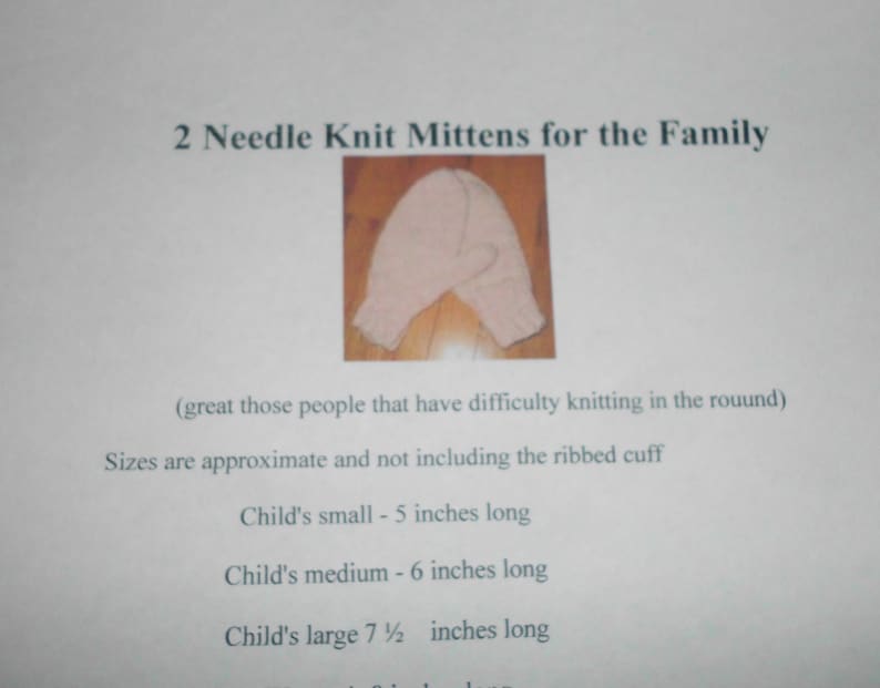 May include: Two pairs of pink knitted mittens for the family. The mittens are shown on a wooden surface. The text on the page reads "2 Needle Knit Mittens for the Family" and includes sizing information for children's mittens: Child's small - 5 inches long, Child's medium - 6 inches long, Child's large 7 1/2 inches long.
