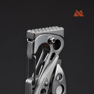 May include: Close-up of a multi-tool with a textured, silver-colored top. The tool has a variety of components, including a blade and other implements. The background is a solid dark gray.