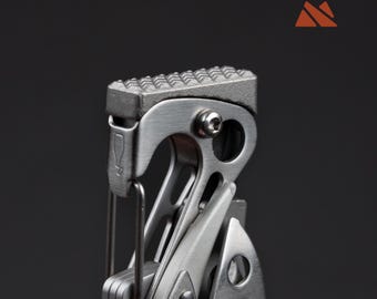 May include: Close-up of a multi-tool with a textured, silver-colored top. The tool has a variety of components, including a blade and other implements. The background is a solid dark gray.