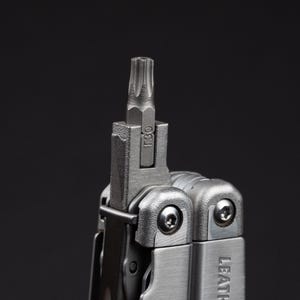 May include: A silver-colored multi-tool featuring a T30 Torx bit extended from the main body. The metal tool has a brushed finish with visible screws and the partial brand name LEATH visible on the side of the handle against a dark background.