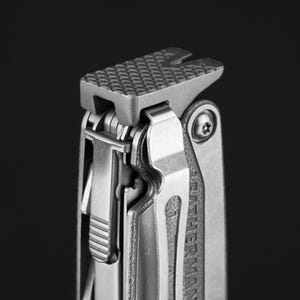 Puede incluir: Una multiherramienta gris que presenta una superficie de martillo texturizada con patrón de cruz en la parte superior. La herramienta incluye un clip de bolsillo de metal plateado en el lateral, con la marca Leatherman grabada en el mango.