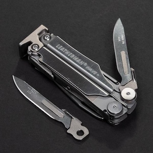 Puede incluir: Una multiherramienta plateada y gris con el texto "LEATHERMAN WAVE+" y dos cuchillas extendidas. La multiherramienta tiene varias herramientas plegadas en su interior. Una cuchilla tiene el texto "HAWAIIN GOA" y la otra "USA".