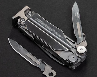May include: A multi-tool with the text "LEATHERMAN WAVE+" and two blades extended. The multi-tool is silver and gray, with a variety of tools folded inside. One blade has the text "HAWAIIN GOA" and the other has the text "USA".
