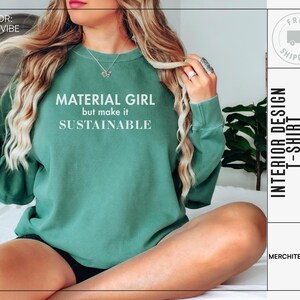 Puede incluir: Una sudadera verde con el texto "MATERIAL GIRL but make it SUSTAINABLE" en blanco. La sudadera la lleva puesta una persona sentada en una cama.