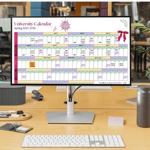 May include: A computer monitor displays a University Calendar for Spring 2025-2026. The calendar is a grid of colored blocks with text. A keyboard, mouse, and other office supplies are on the wooden desk.