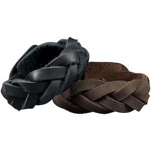 May include: Two braided leather bracelets, one in black and one in dark brown. Each bracelet features a thick, woven design with a smooth outer surface and a textured inner side, showcasing the natural grain and edges of the leather material.