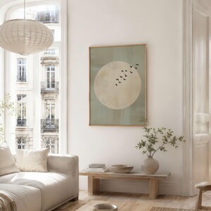 May include: A framed art print featuring a large, pale yellow circle with a flock of black birds in flight against a muted green background. The artwork is displayed in a light-colored wooden frame, adding a touch of nature-inspired decor.