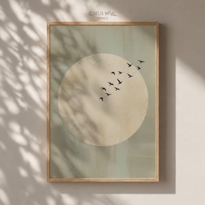 May include: A framed wall art print featuring a large, textured beige circle centered on a muted sage green background. A flock of small black birds is depicted flying diagonally across the upper right portion of the circle. The text LOTUS WALL PRINTS is visible at the top center of the print.