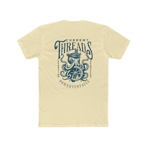 Op de afbeelding: Crèmekleurig T-shirt met een marineblauwe octopus die een kapiteinshoed draagt en een scheepsstuur vasthoudt. De tekst "CURRENT THREADS" staat erboven, met "ESTD 2025 POWERTENTACLE" eronder.
