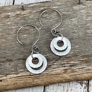 Op de afbeelding: Een paar zilveren oorbellen met twee gehammerde metalen cirkels die aan een zilveren haak hangen.