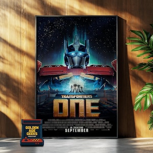 Pode incluir: Um poster emoldurado do filme "Transformers: ONE" com Optimus Prime. O poster tem um fundo escuro com o título em dourado e o mês de lançamento, setembro. Um jogo de arcade retrô está em primeiro plano.