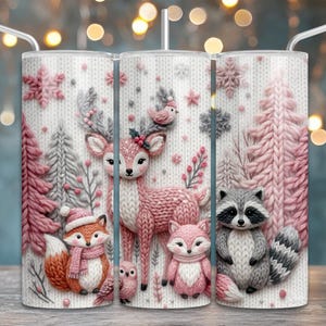 May include: A white tumbler with a winter forest scene featuring a deer, fox, raccoon, and owl. The design includes pink and gray knitted trees, snowflakes, and woodland creatures. The tumbler has a silver straw.