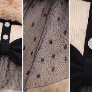 May include: A cream-colored pet dress with a black bow and a black collar. The dress features a black polka dot tulle skirt and pearl-like buttons. The dress is designed for a small dog or cat.