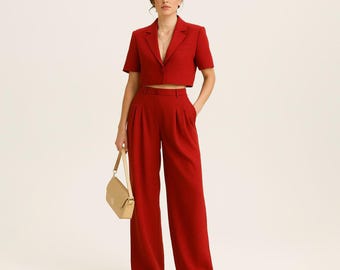 Pode incluir: Um conjunto vermelho de duas peças com um blazer curto de mangas curtas e calças de perna larga. O conjunto é combinado com uma bolsa de ombro bege e sapatos rasos a condizer. A roupa é de cor sólida, criando um visual coeso e elegante.