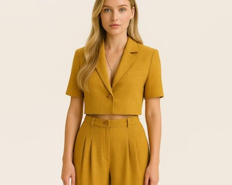 Pode incluir: Conjunto mostarda composto por um blazer de manga curta e calças de cintura alta a condizer. O blazer tem lapelas entalhadas, fecho de um botão e um pequeno bolso. As calças têm a frente plissada e fecho de botão.