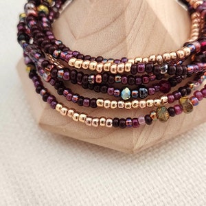 May include: A multi-strand bracelet made of small, colorful beads. The bracelet features a mix of burgundy, gold, and iridescent beads.