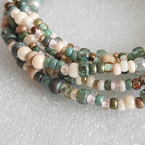 May include: A multi-strand bracelet made with small, colorful beads in shades of green, brown, and white. The beads are arranged in a random pattern, creating a unique and eye-catching design.