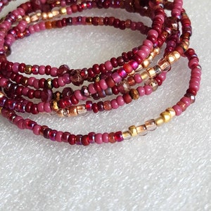 May include: Close-up of several strands of beaded jewelry in shades of red, burgundy, and gold. The beads are small and round, with some faceted for added sparkle. The jewelry is likely a bracelet or waist beads.