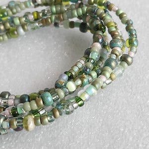 May include: A close-up of a multi-strand beaded bracelet with green, blue, and white beads. The bracelet is made of small, round beads and has a delicate, feminine look.