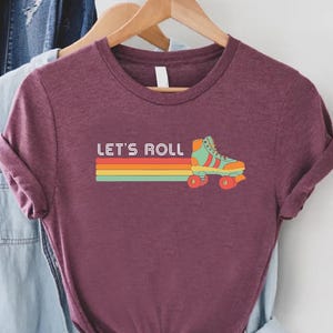 May include: A maroon t-shirt with a retro roller skate graphic and the text "Let's Roll" in rainbow colors.