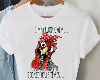May include: White t-shirt with a graphic of a red and black chicken wearing red glasses and a red and white polka dot bandana. The text on the shirt reads "I may look calm... But in my head I've pecked you 3 times..."