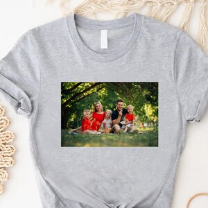 May include: A gray t-shirt with a photo of a family of five in a park setting. The family is smiling and wearing casual clothing. The photo is printed on the front of the shirt.