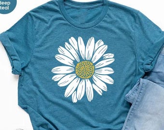 May include: A teal blue t-shirt with a white daisy graphic. The daisy has a yellow center with green accents.