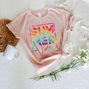 May include: A pink t-shirt with a tie-dye design that says "Summer vibes" in a white box.