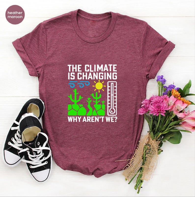 May include: Heather maroon t-shirt with the text "THE CLIMATE IS CHANGING WHY AREN'T WE?" and a graphic of a sun, thermometer, and cacti. Black and white sneakers are on the left. A bouquet of flowers is on the right.