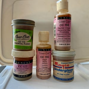 May include: Five bottles of Duncan Cover-Coat opaque underglaze paint in various colors, including Oriental Flesh, Moonstone Grey, Peach, Peaches 'n Cream, and a bottle of Mayco Underglaze Color in Pink Flesh. Each bottle is 2 fluid ounces.