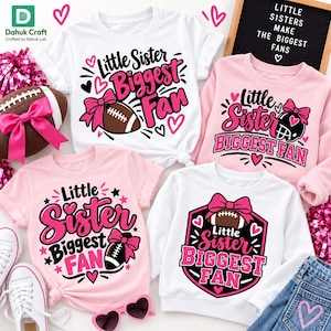 Puede incluir: Cuatro camisetas con el texto Little Sister Biggest Fan en rosa y negro. Los diseños incluyen balones de fútbol con lazos rosas, corazones y estrellas. Dos son blancas y dos son rosa claro, con variaciones en la disposición de los gráficos.